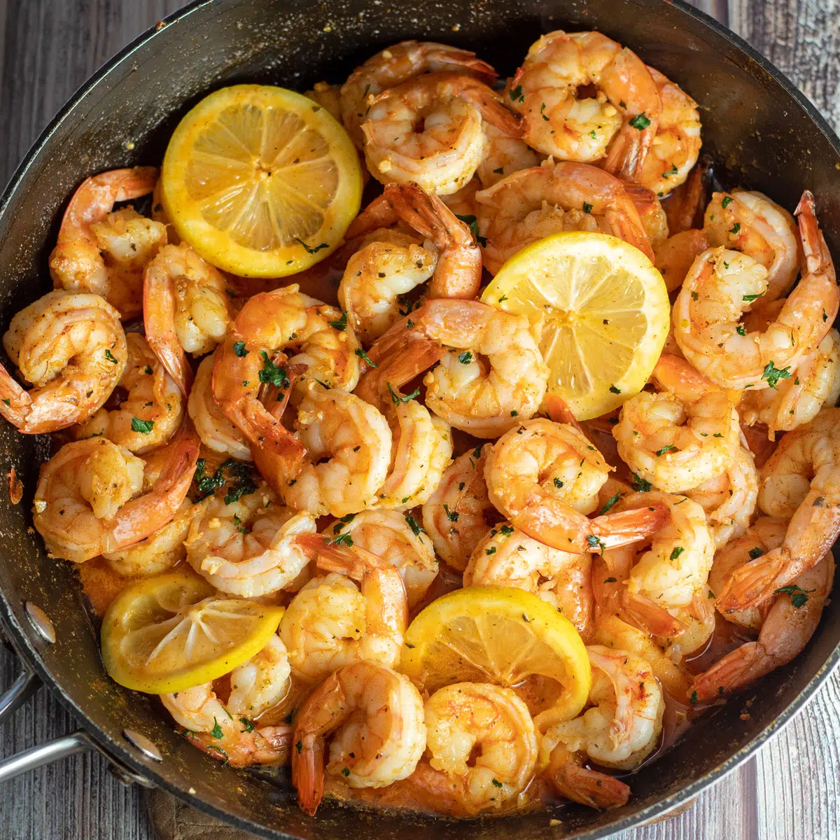 Square image of cajun shrimp with lemon slices in a frying pan.