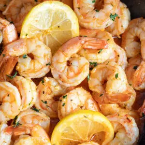 Closeup square image of cajun shrimp with lemon slices in a frying pan.