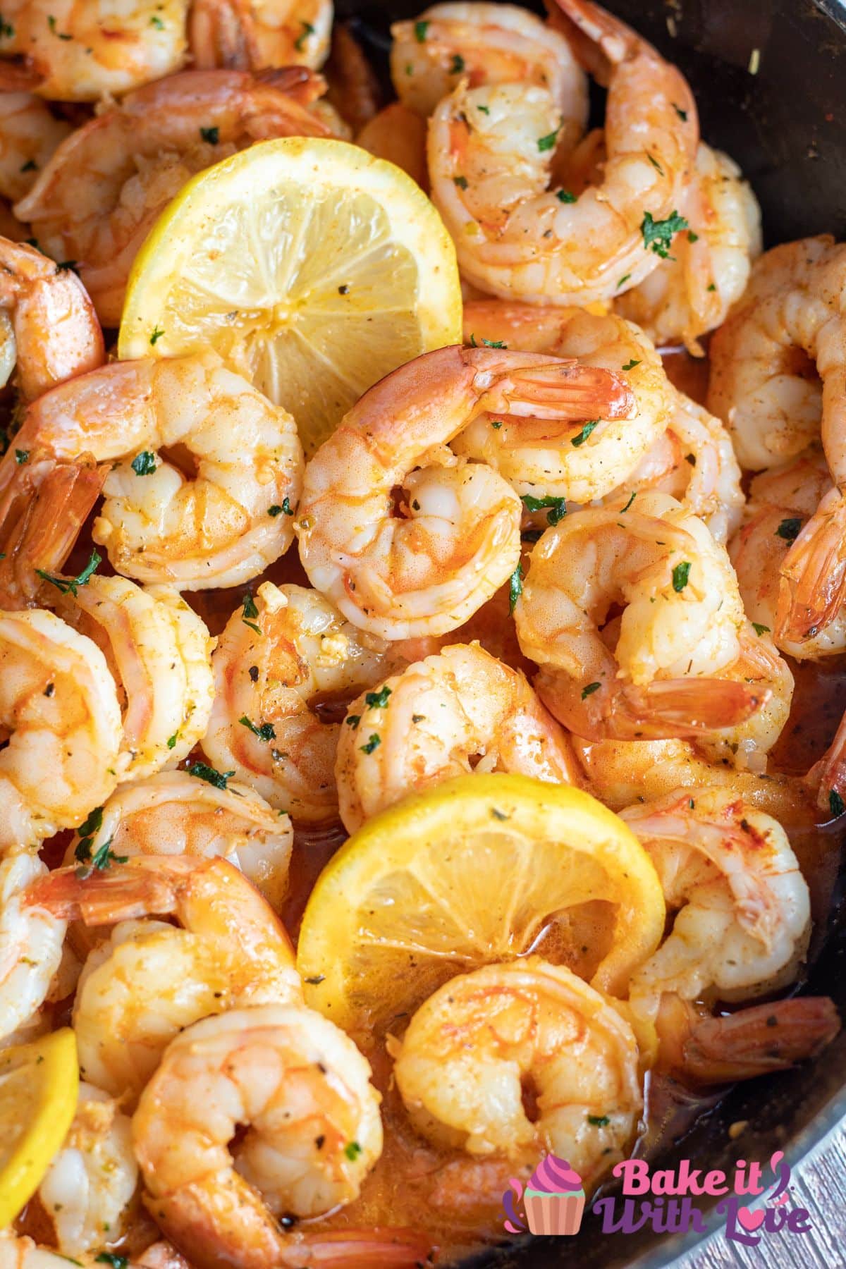 Tall image of cajun shrimp with lemon slices in a frying pan.