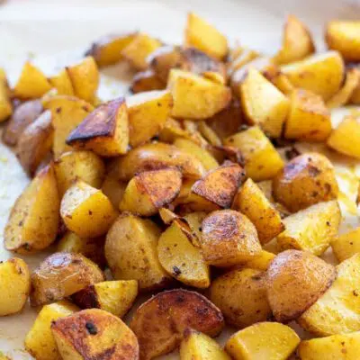 Tall image of curry roasted potatoes on a baking sheet.