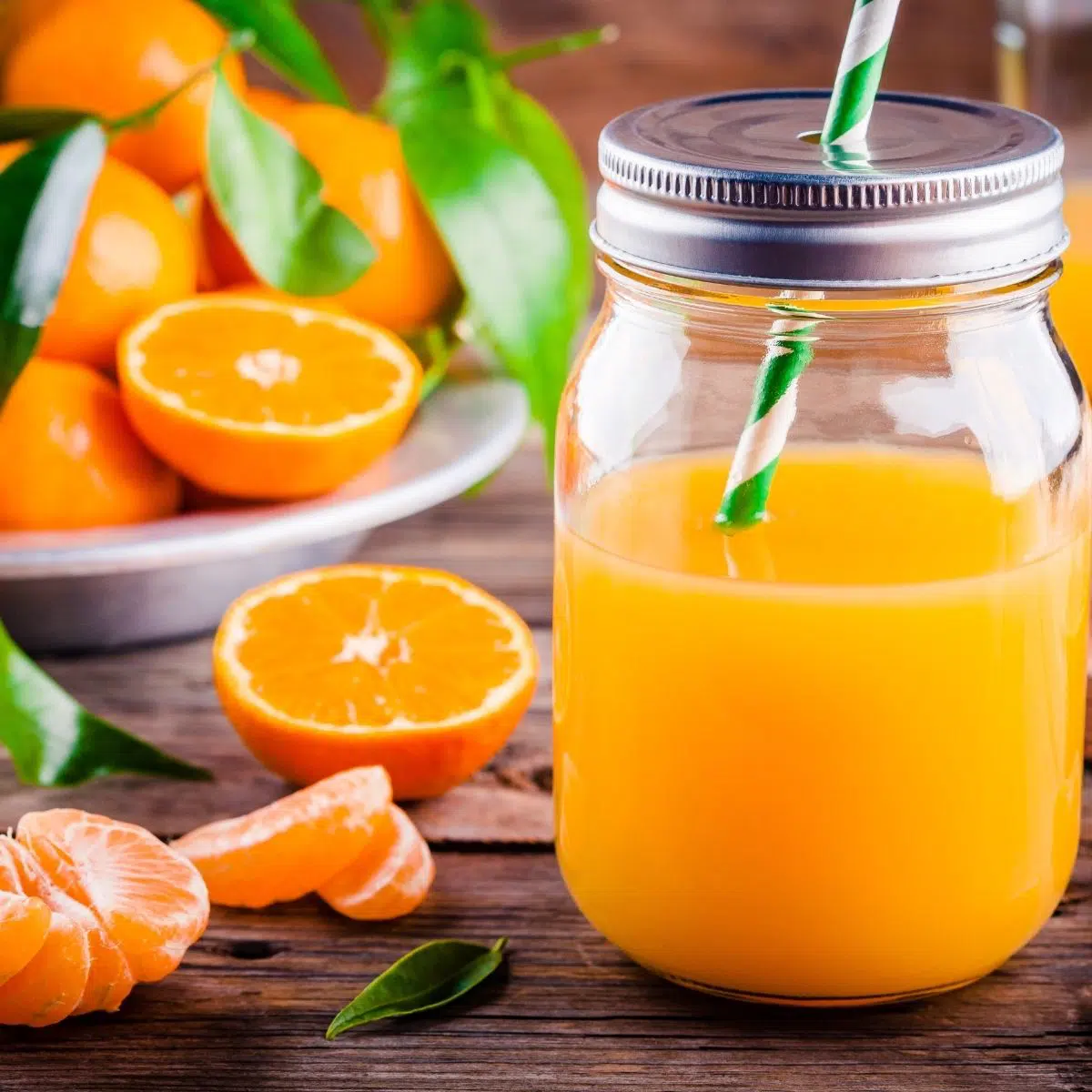 Square image showing orange juice and peeled orange fruit.