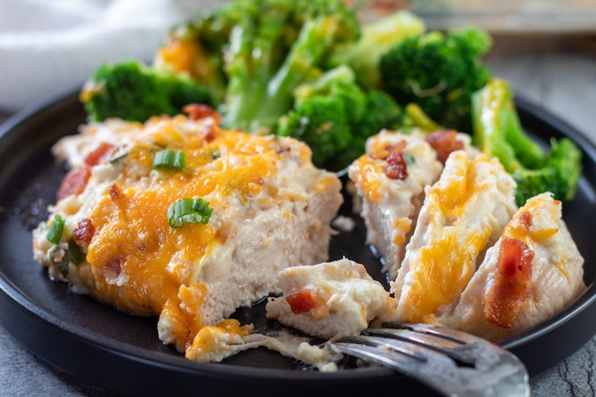 Wide image of baked million dollar chicken cut open on a plate.