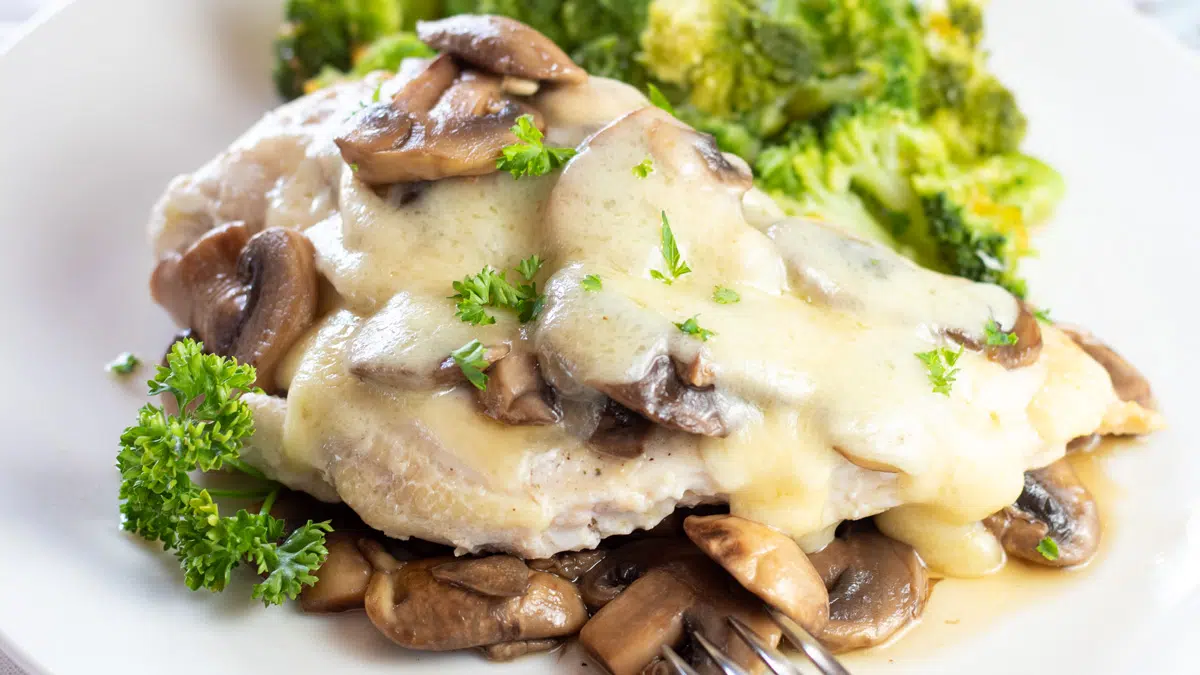 Wide closeup on the mushroom swiss chicken on white plate garnished with fresh parsley.