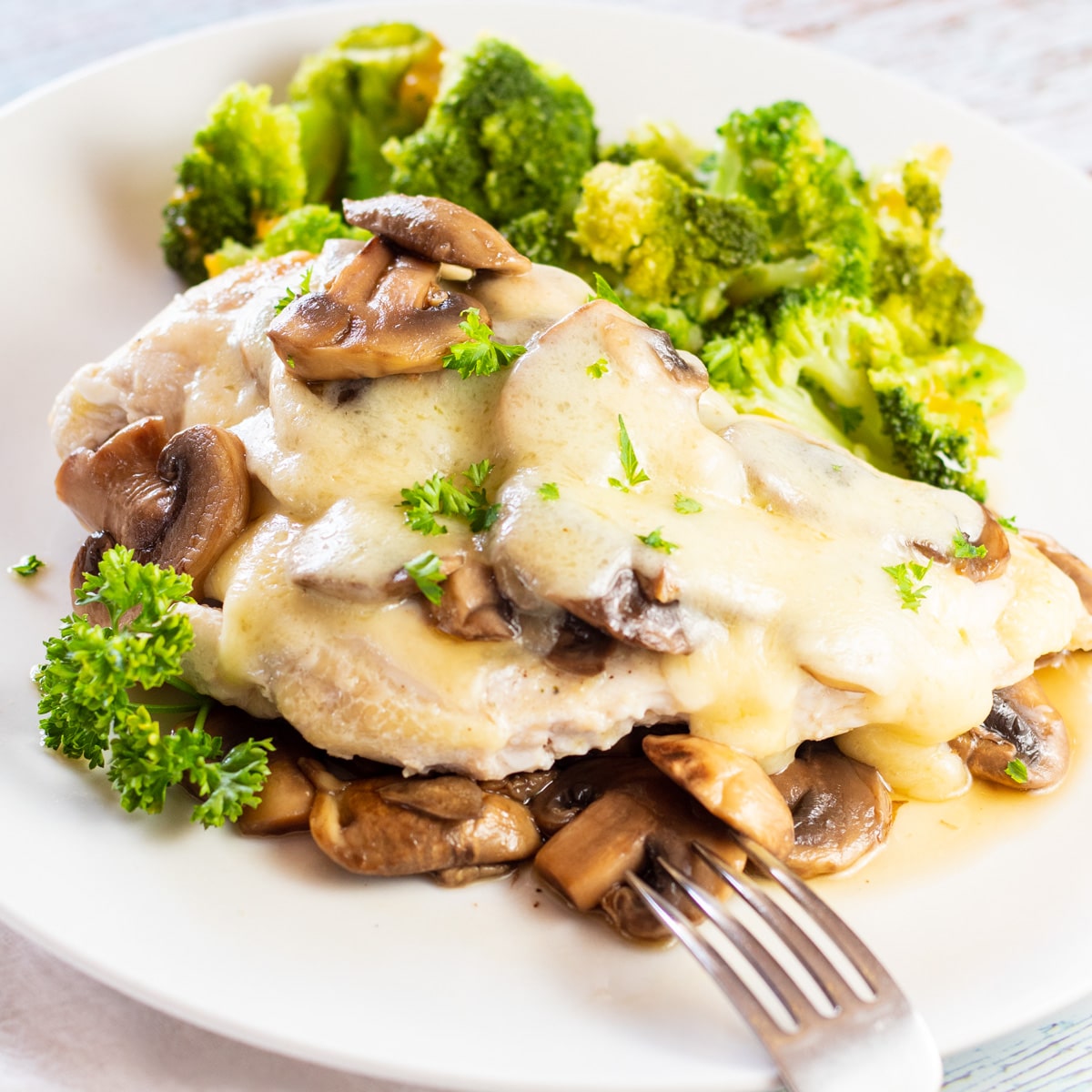 Křehké, chutné houbové švýcarské kuře se podává přes další restované houby na bílém talíři.