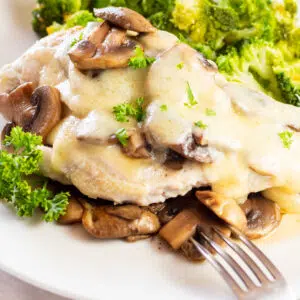 Closeup on th eplated mushroom swiss chicken breast on white plate with fork.
