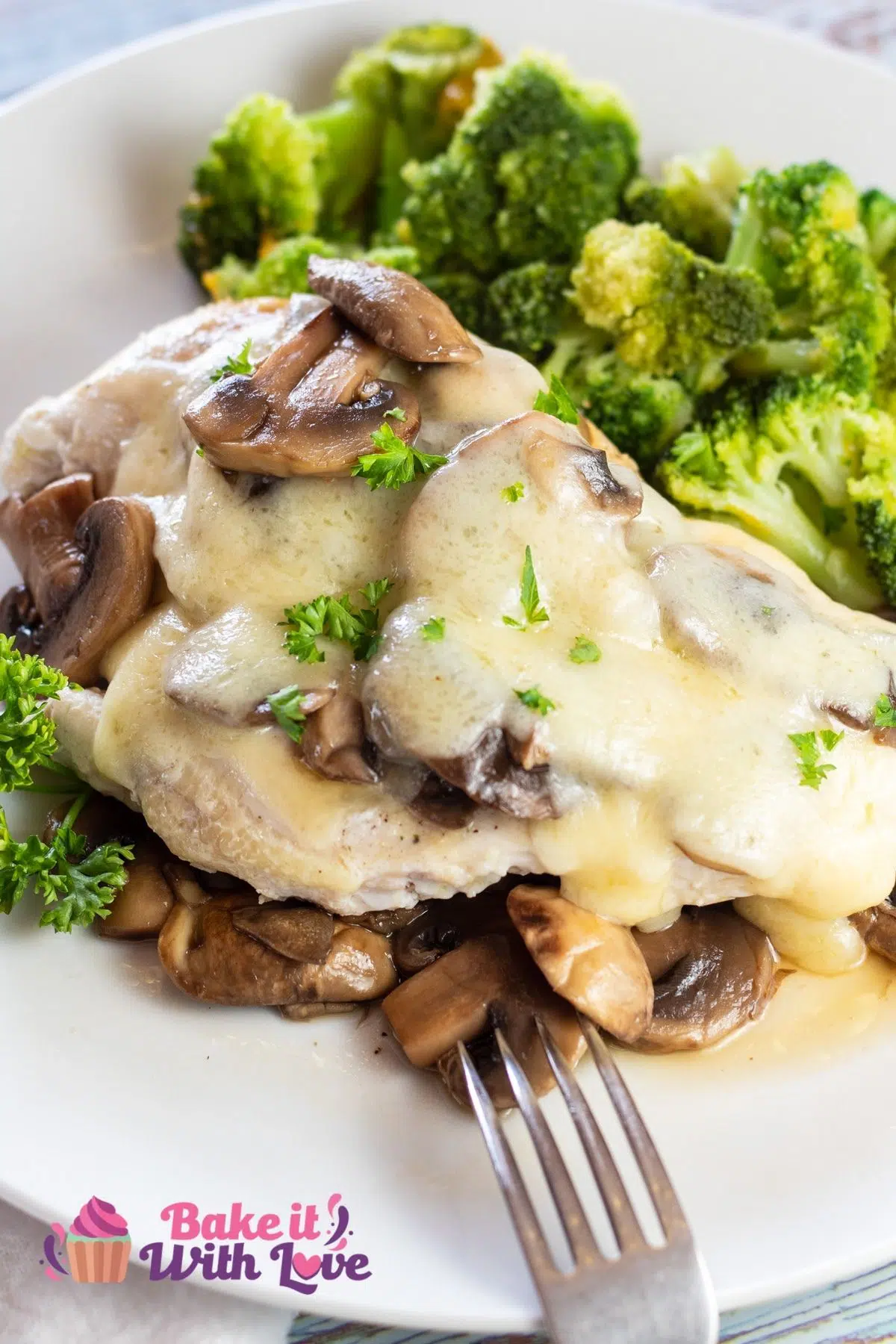 Tall closeup on the plated mushroom swiss chicken served with sauteed mushrooms, melted swiss cheese, and broccoli.