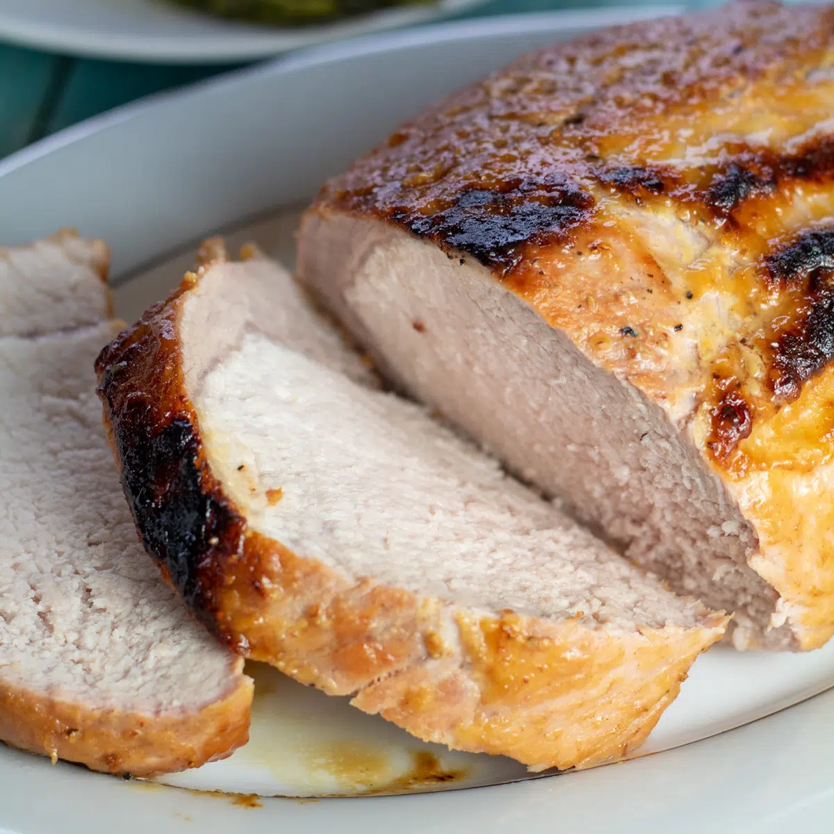 Imagen cuadrada de chuletón de cerdo asado, rebanado en un plato con patatas y espárragos.