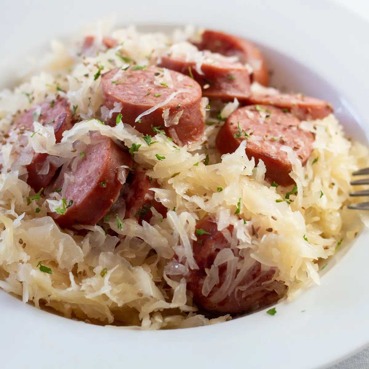 Tasty slow cooker kielbasa and sauerkraut is served up ready to eat in a white bowl.