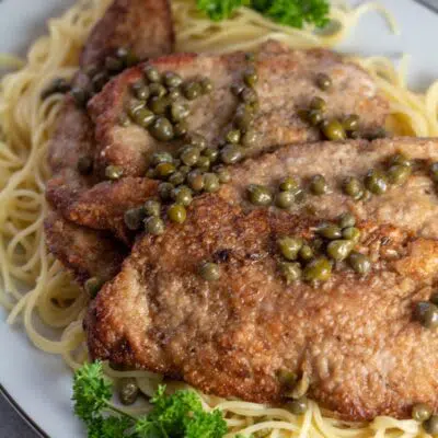 Pin image with text of veal scallopini on a bed of pasta.