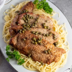 Square image of veal scallopini on a bed of pasta.