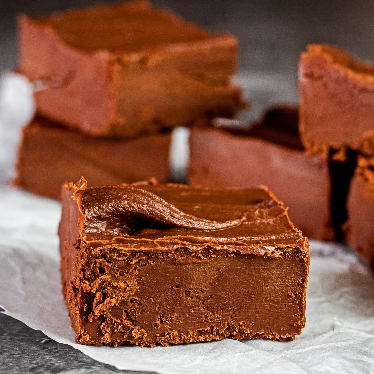 Closeup on the tasty chocolate frosting fudge squares stacked on parchment paper.