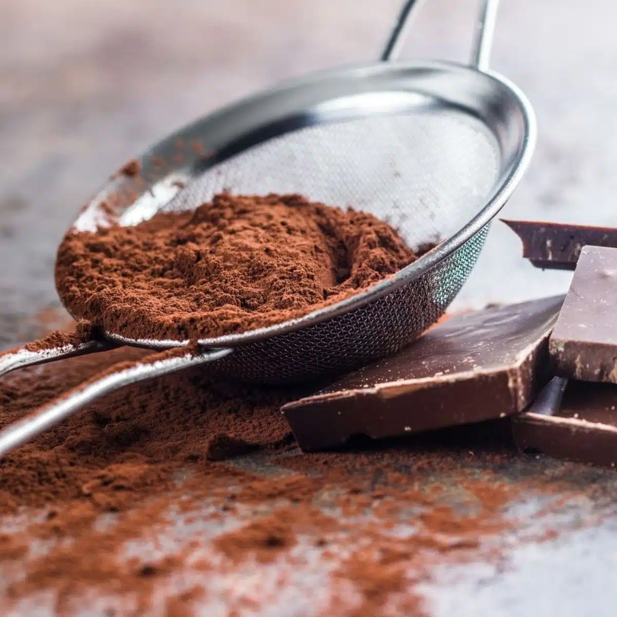 Sostituto del cacao in polvere con l'immagine del cacao sfuso in un colino a maglia fine.