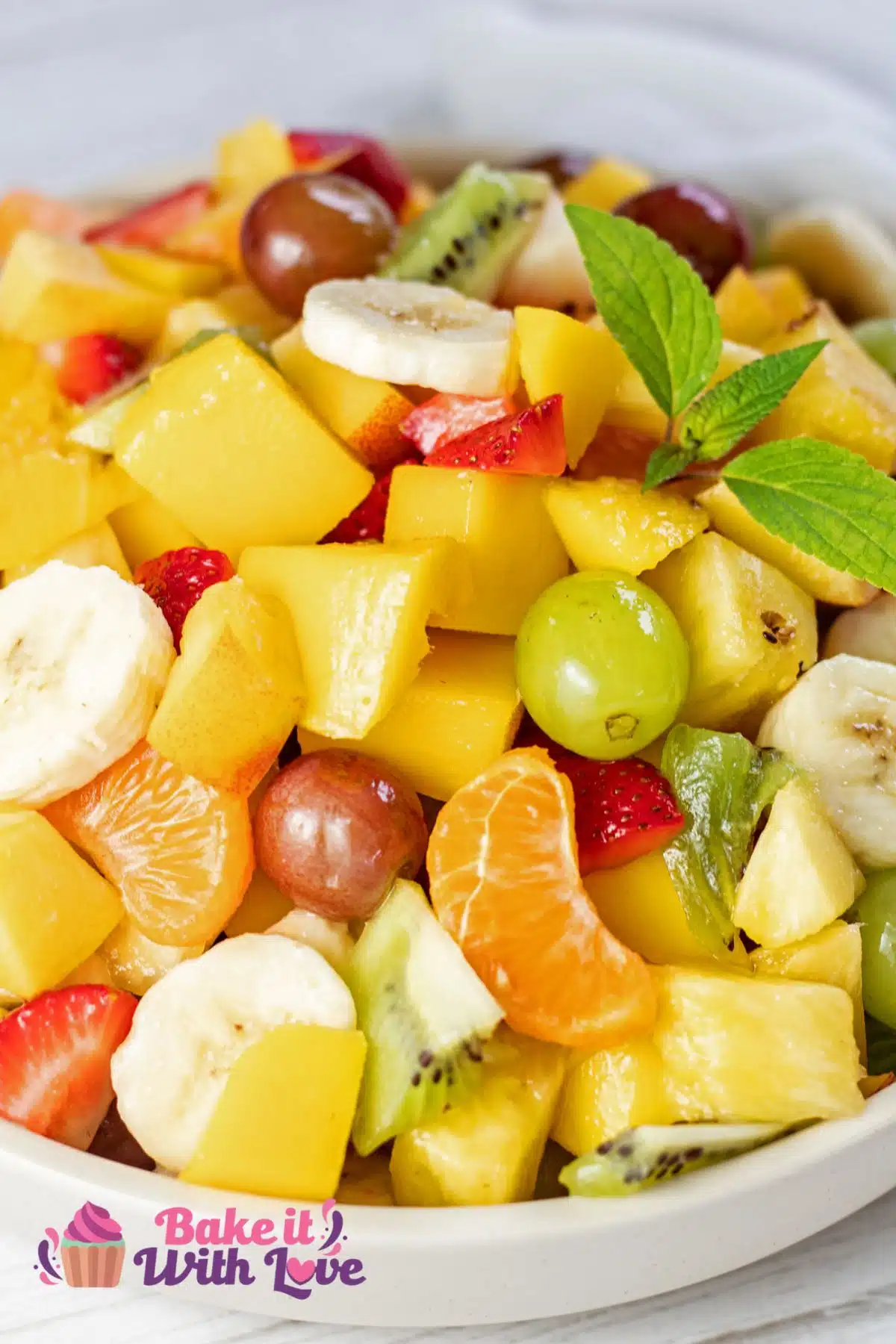Tall closeup on the assembled fresh fruit salad in white serving bowl.