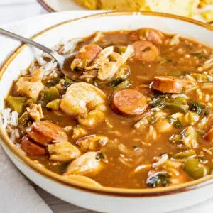 Closeup of the dished up gumbo soup with white rice in it, cornbread in the background, and a spoon off to the side.