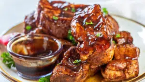 Wide closeup on the slow cooker country style pork ribs served on tan plate with extra bbq sauce on the side.