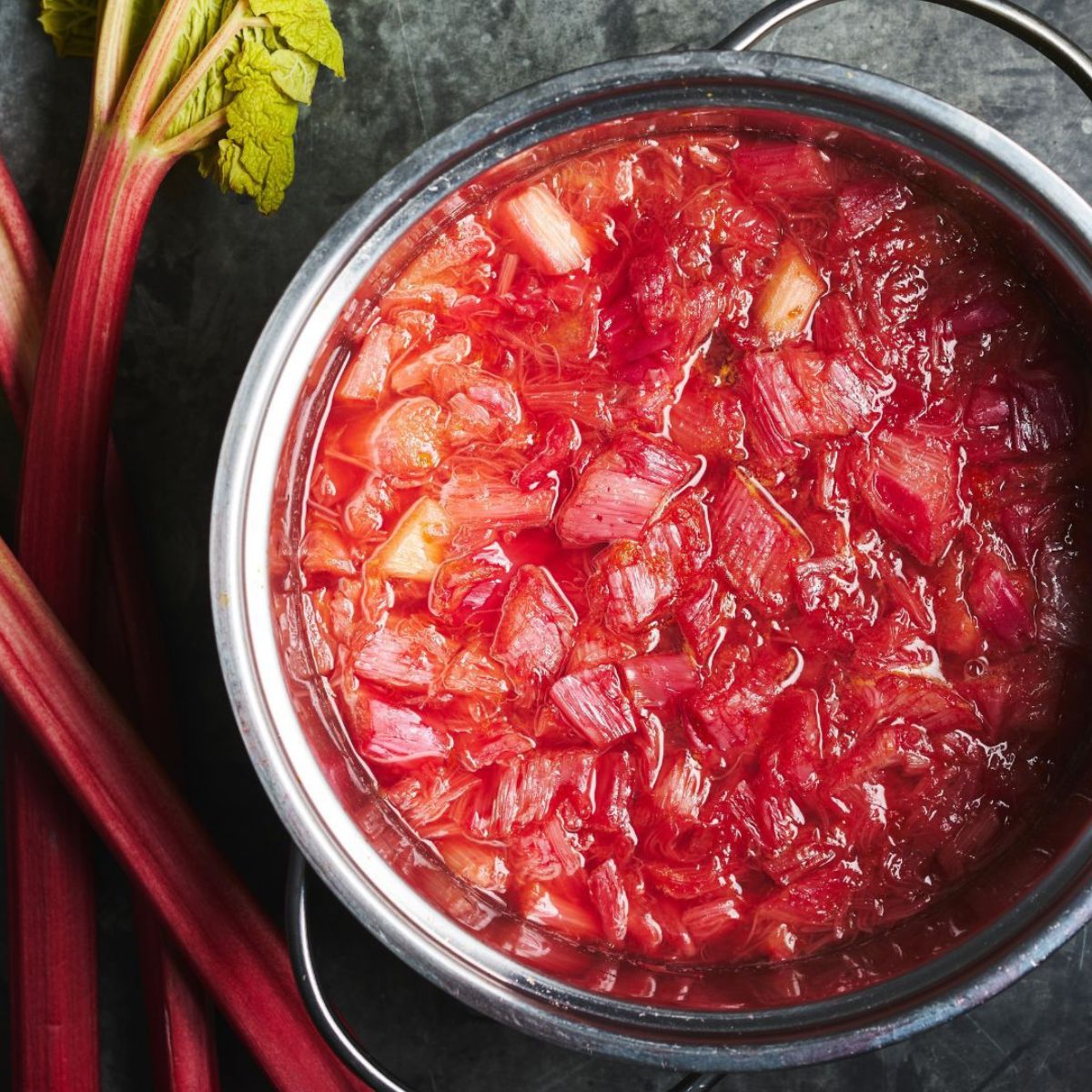 Stewed rhubarb in stainless steel pot with rhubarb stalks on the side.