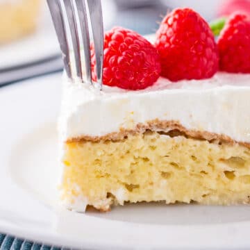 Best homemade tres leches cake with raspberries on top and a fork about to cut away a bite.