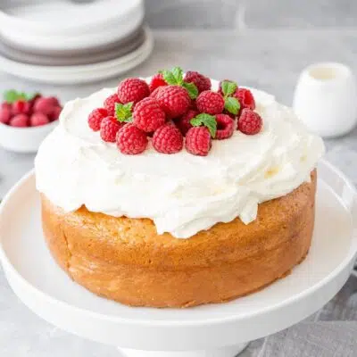 Best tres leches cake served on white platter and topped with heavenly whipped cream and raspberries.