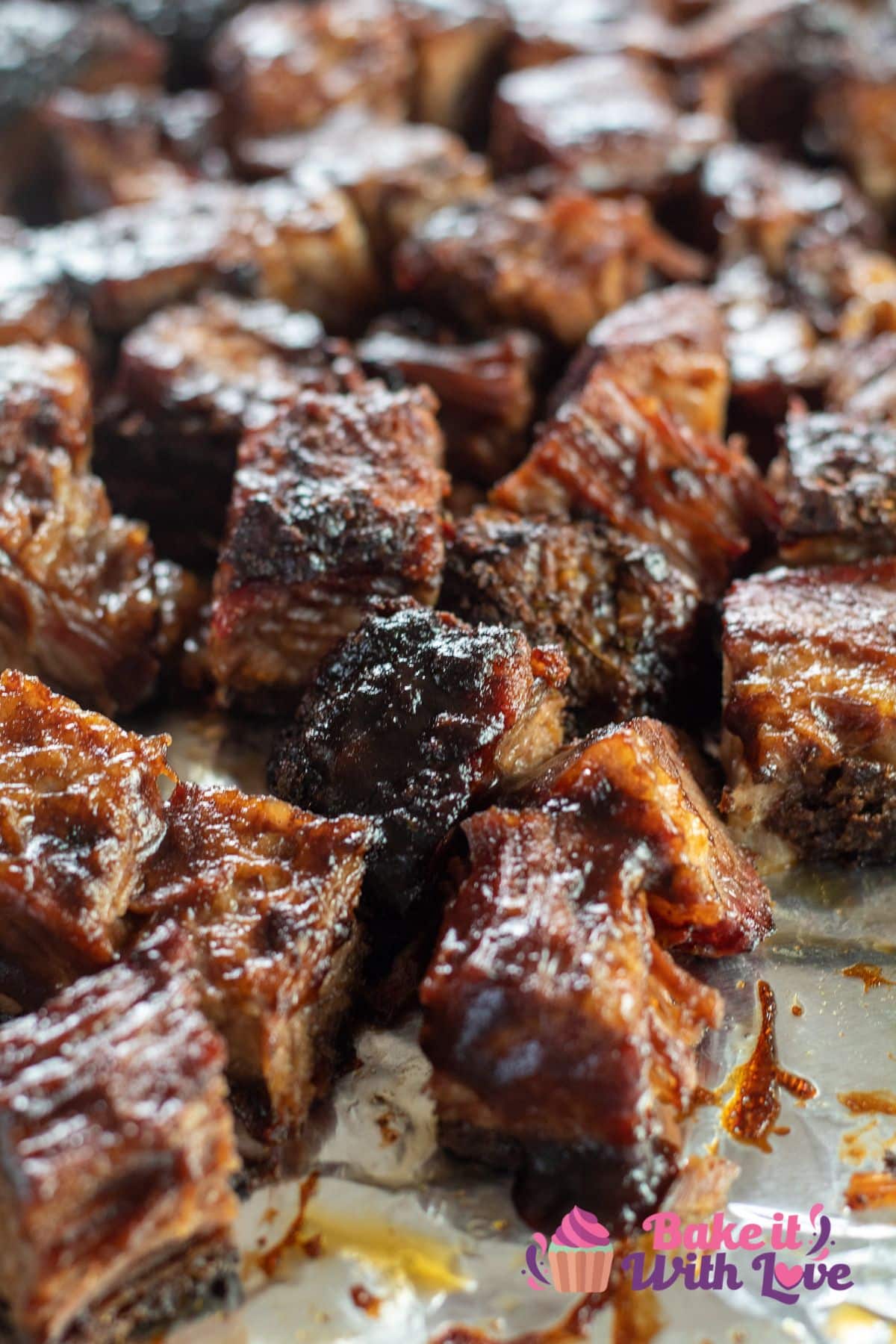 Tall closeup of the brisket burnt ends in smoking tray coated with plenty of BBQ sauce.
