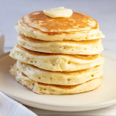 A tall stack of fulffy buttermilk pancakes with a pat of butter on top.