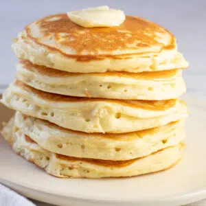 A stack of perfect fluffy buttermilk pancakes on off white plate.