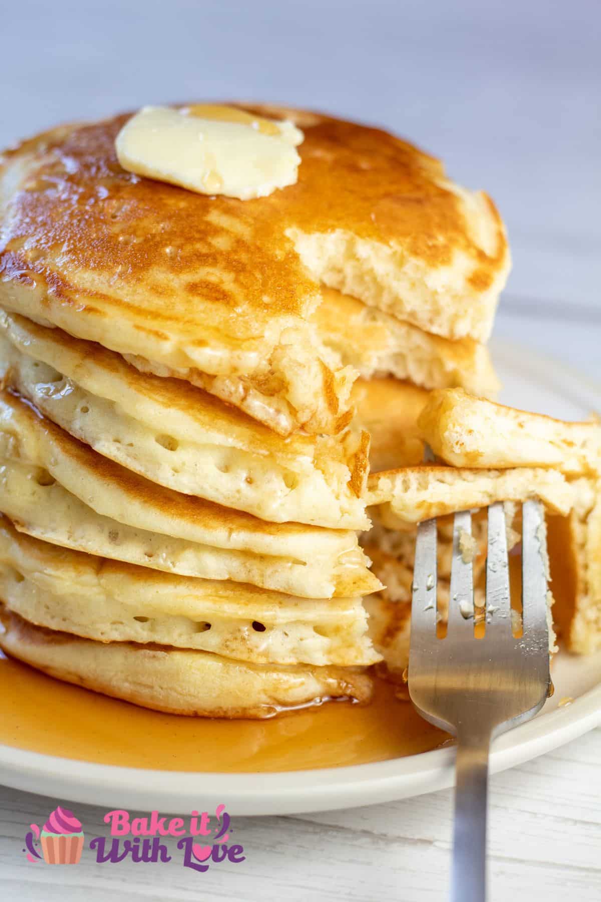Tall stack of buttermilk pancakes with syrup and a bite cut through the stack.