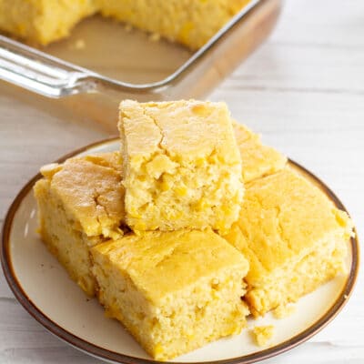 Creamed corn cornbread sliced into squares and stacked on tan plate.