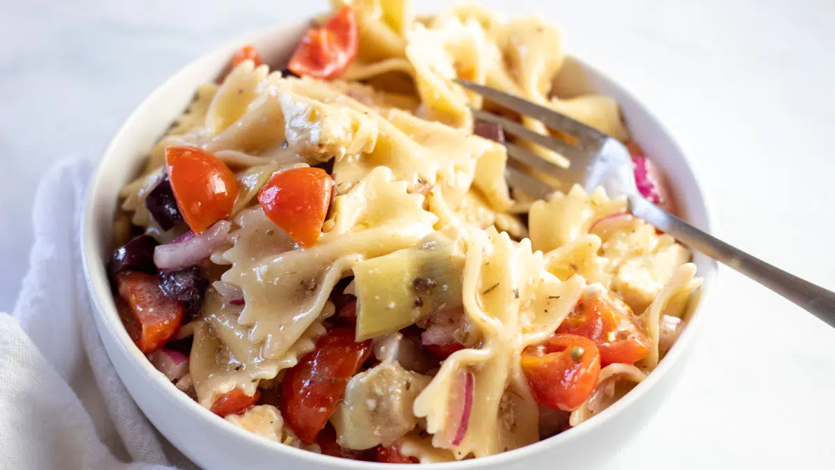 Wide image of a white bowl full of Greek pasta salad.