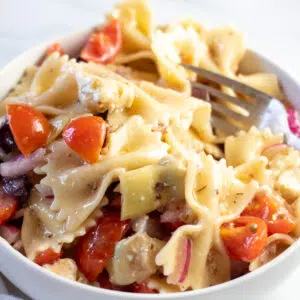 Square image of a white bowl full of Greek pasta salad.