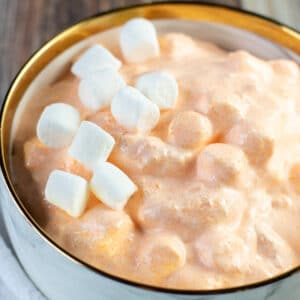 Square image of mandarin orange jello salad in a bowl with marshmallows.