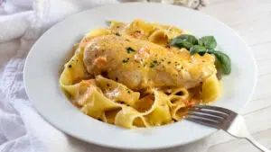 Wide image of marry me chicken over pasta in a white dish.