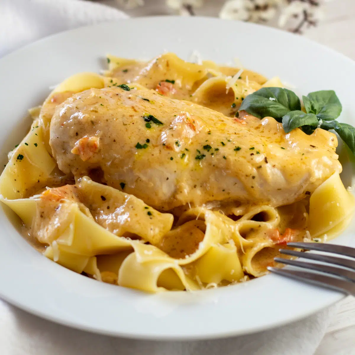 Square image of marry me chicken over pasta in a white dish.