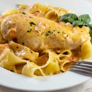 Close up square image of marry me chicken over pasta in a white dish.