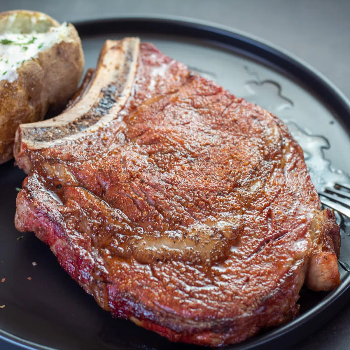 Flavorful, perfectly smoked ribeye steak on black plate with potato.