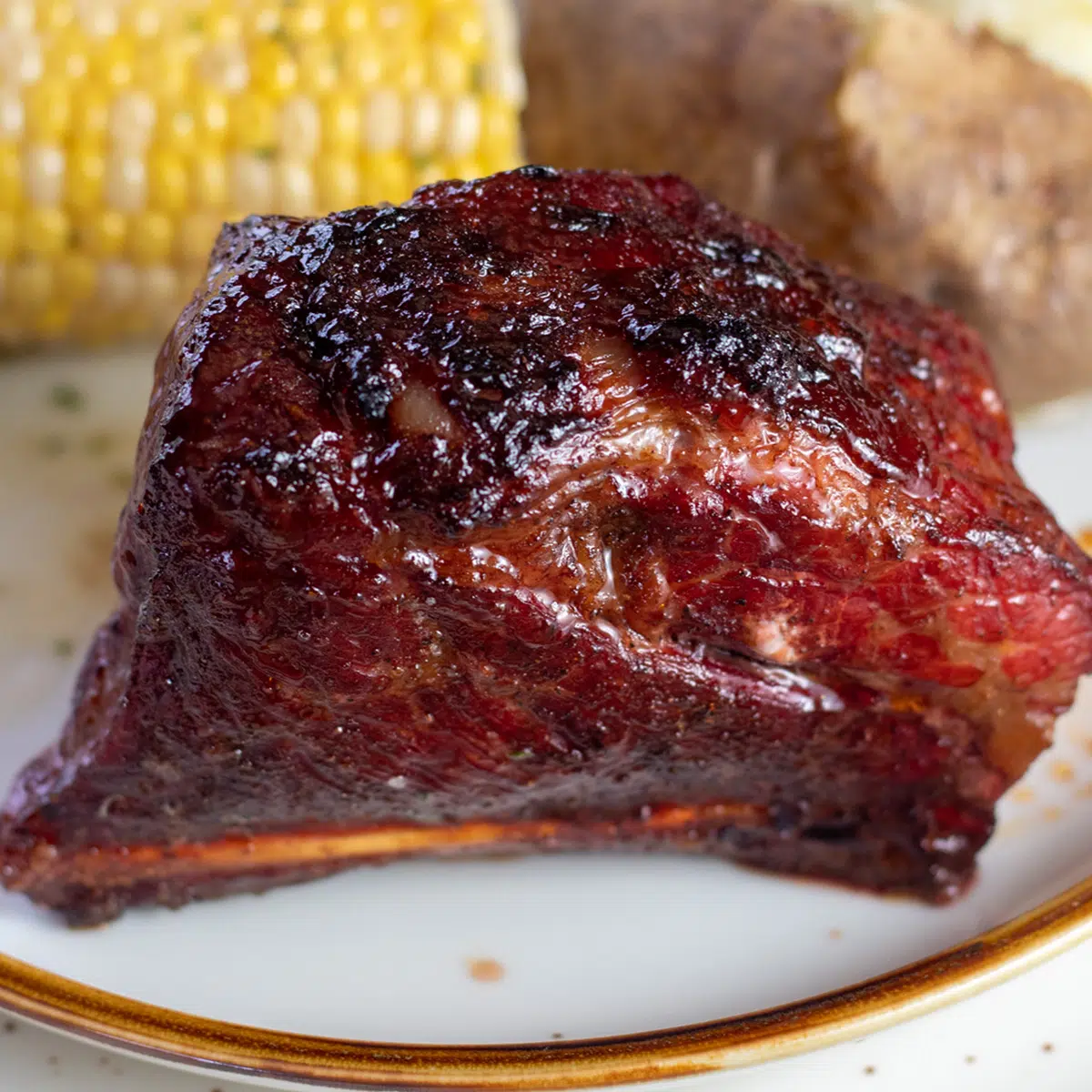 Smoked short ribs served on tan plate with potato and corn on the cob.