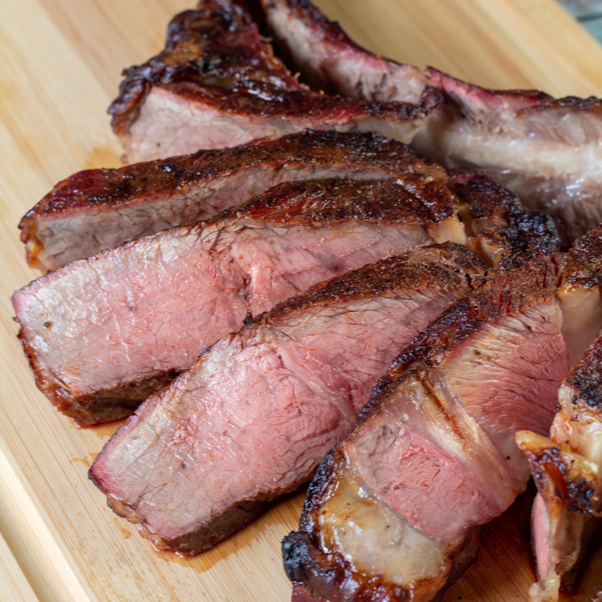 Square image of sliced smoked tomahawk steak on a cutting board.
