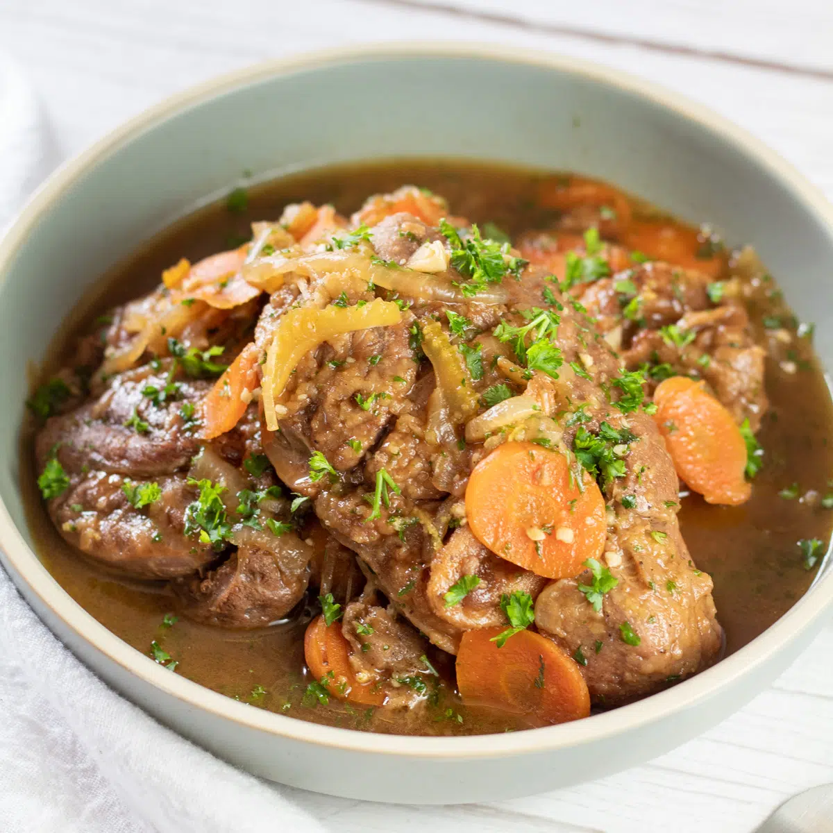 Square image of a bowl of veal osso buco all milanese.