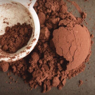 Cocoa vs cacao powder, differences and similarities listed and compared with loose cocoa powder on dark surface.