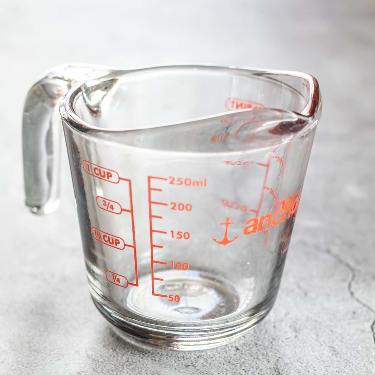 How many milliters ml in a cup with a glass pyrex liquid measuring cup on light surface.