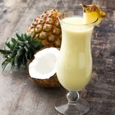 Creamy, tasty pina colada mocktail in tall hurricane glass garnished with pineapple wedge.