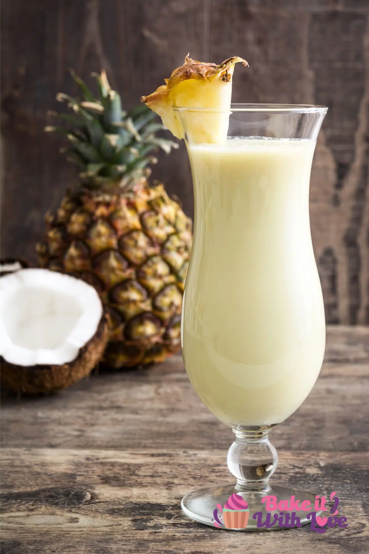 Tasty pina colada mocktail that everyone can enjoy, served in a tall hurricane glass with pineapple and coconut in background.