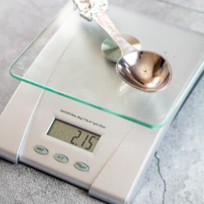 How many tablespoons in an ounce image with metal tablespoon on kitchen scale.