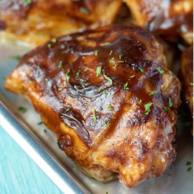 Square image of bbq baked chicken thigh on a small baking sheet.