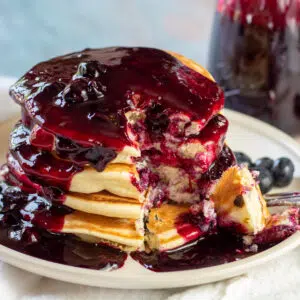 Close up square image of blueberry pancakes with blueberry syrup on a plate.