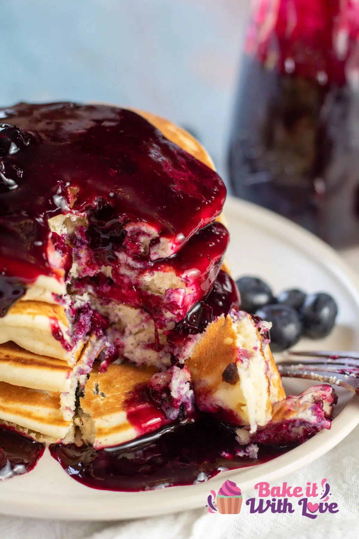 Tall image of blueberry pancakes with blueberry syrup on a plate.