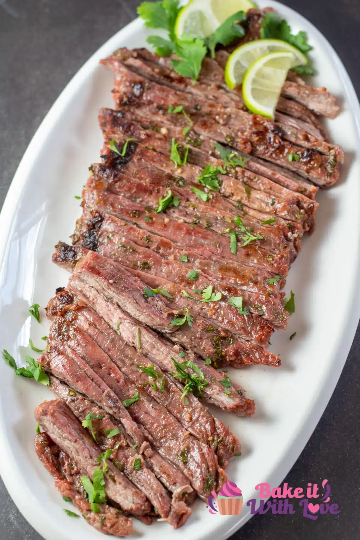 Tall image showing carne asada with sliced limes on a white serving platter.