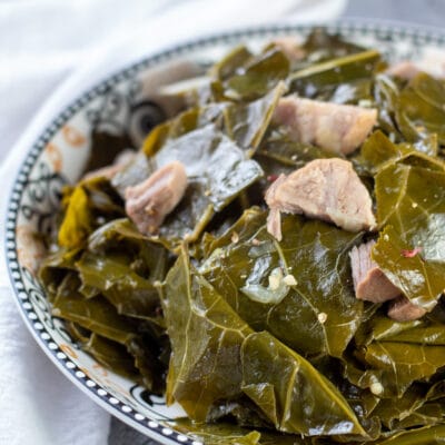 Square image of collard greens with ham hocks in a serving bowl.