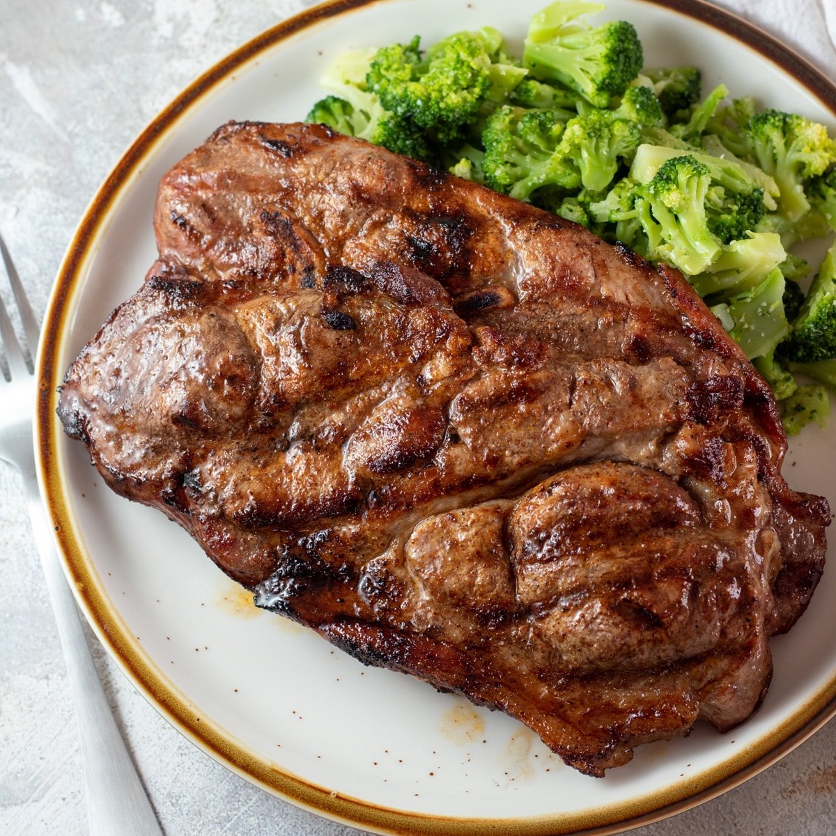 Juicy grilled pork steaks on a tan plate with steamed broccoli.