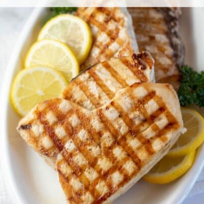 Pin image with text of grilled swordfish on a white plate with fresh lemon slices.