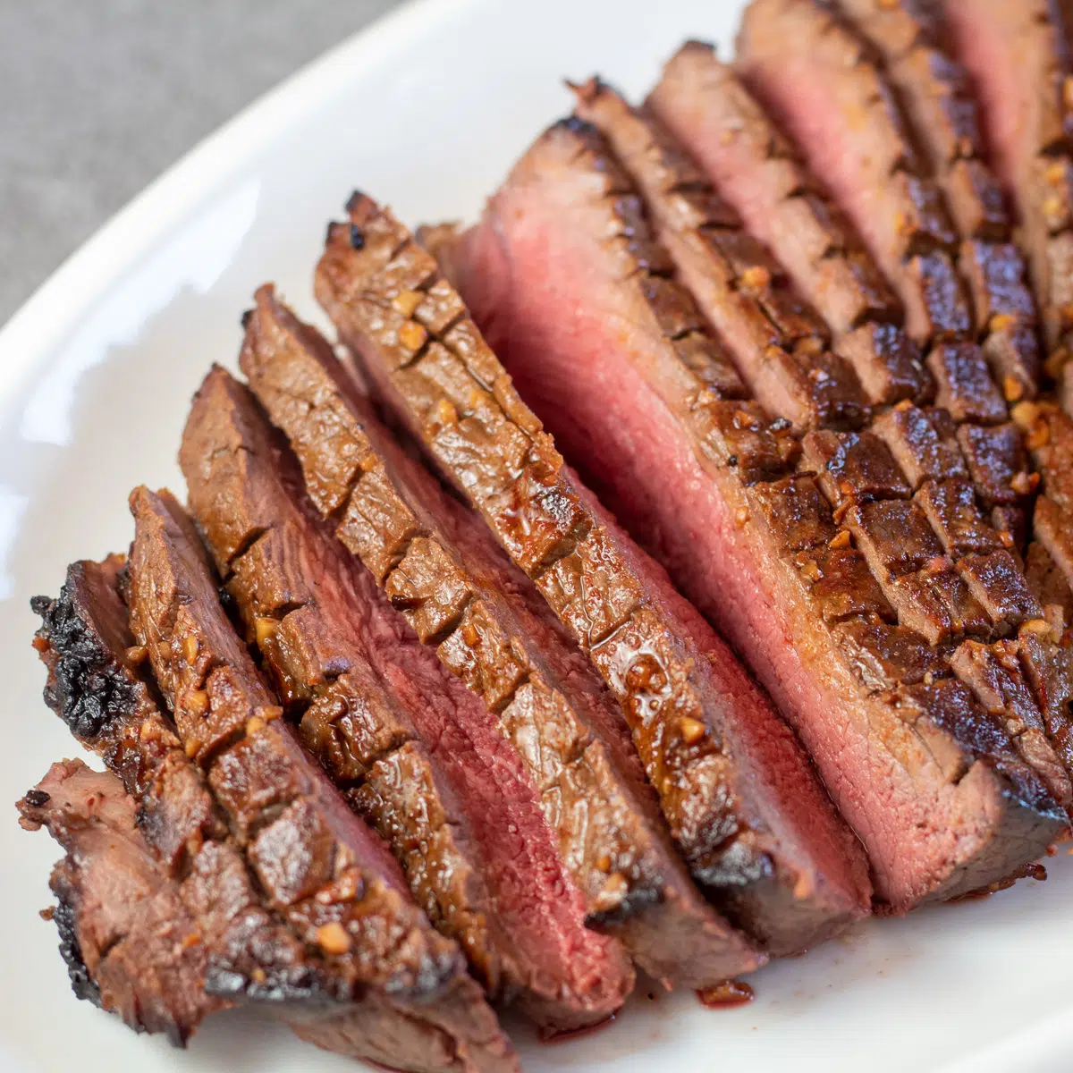 Square image of classic London broil on a white platter.
